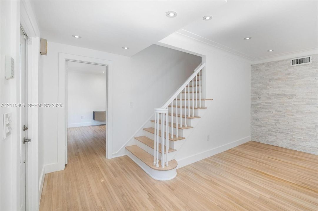 Staircase featuring white balusters and wood-finish treads, natural wood-finish flooring, recessed lighting, and a floor-to-ceiling stacked stone accent wall