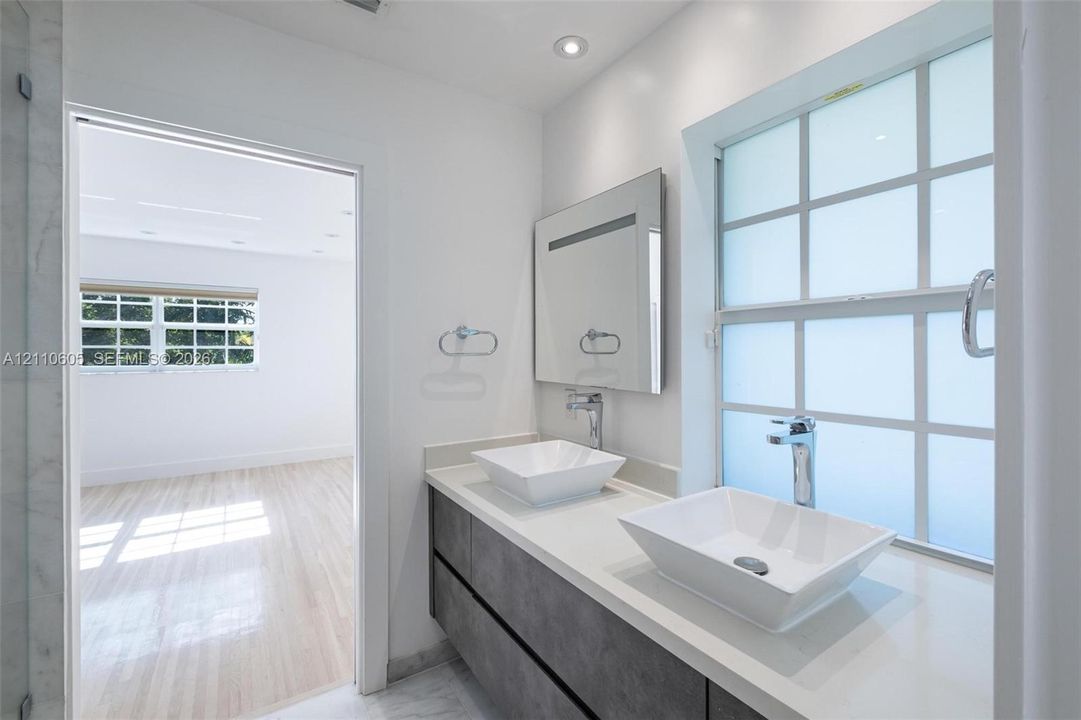 Floating vanity featuring dual rectangular vessel sinks, a solid-surface countertop, modern chrome hardware, and a grid-patterned privacy window