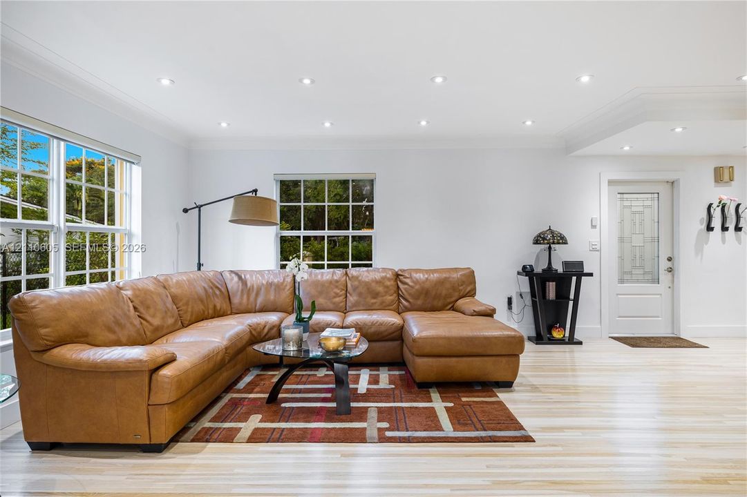 Living area featuring light-toned wood-finish flooring, recessed lighting, multi-pane windows, and a glass-paneled entry door