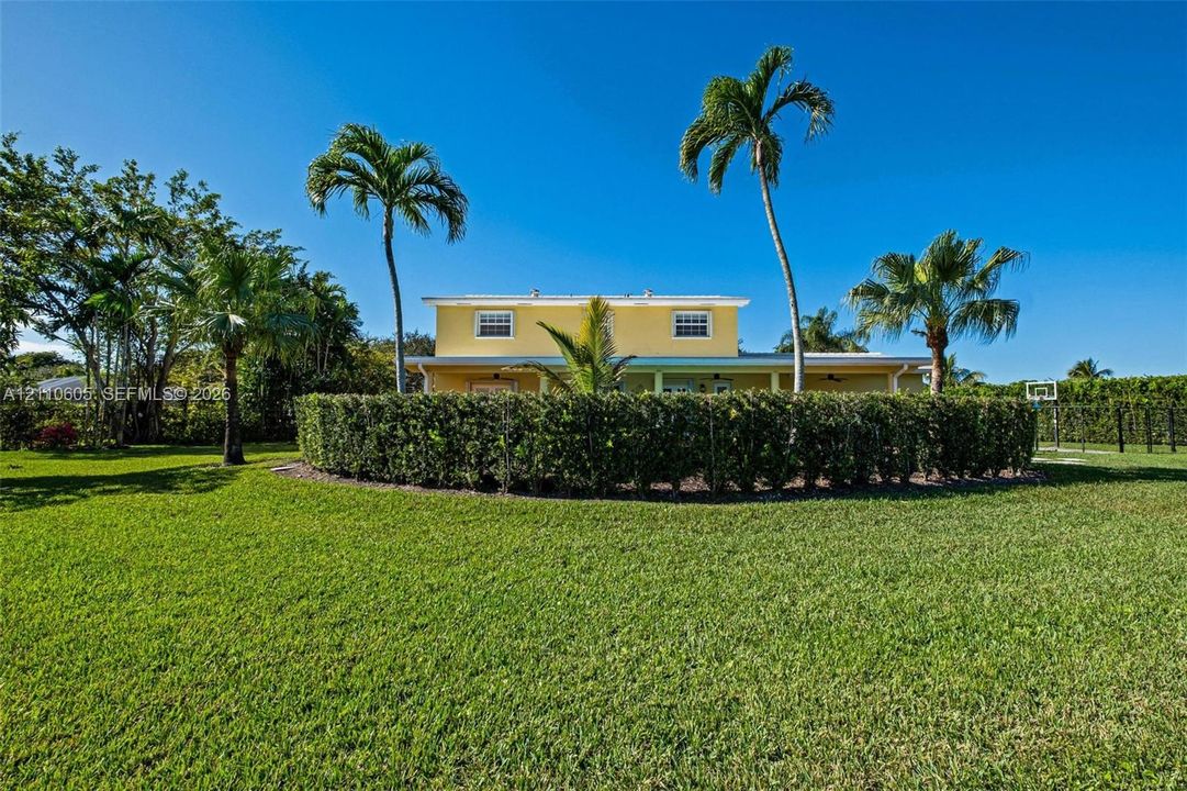 Expansive lawn featuring perimeter hedge landscaping, mature palm trees, and a two-story exterior