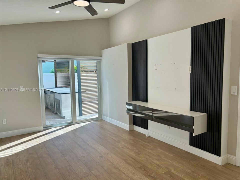 Vaulted ceilings, wood-finish flooring, and a custom accent wall featuring vertical slat detailing with a wall-mounted floating console