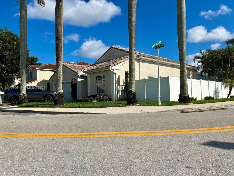 Stucco exterior featuring a tiled roof, concrete driveway, and white vinyl perimeter fencing