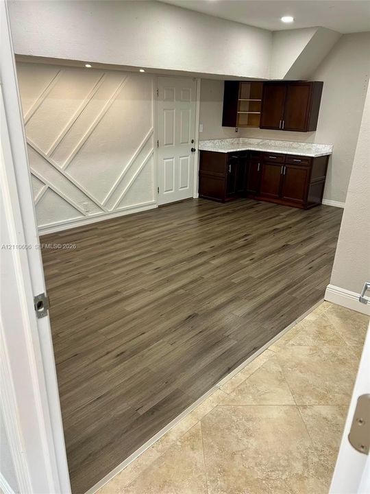 Geometric wall molding, wood-finish flooring, dark-stained cabinetry, light-toned stone-finish countertops, and recessed lighting