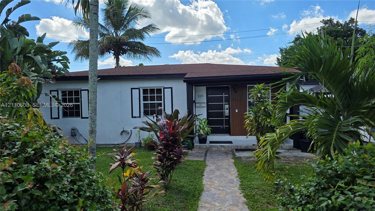 Single-story residence featuring a smooth stucco facade, asphalt shingle roof, modern entry door with horizontal glass panels, decorative exterior shutters, and a natural stone walkway