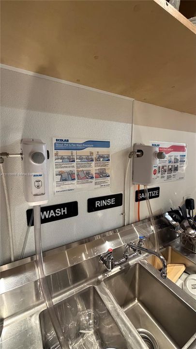 Stainless steel multi-compartment sink featuring wall-mounted chemical dispensing systems and dedicated sanitation stations