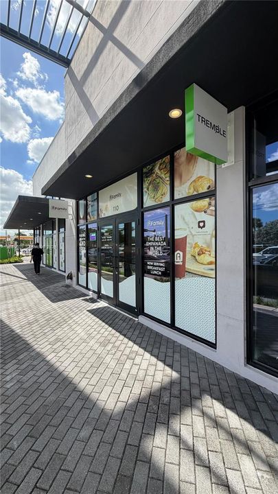 Commercial storefront featuring floor-to-ceiling glass windows, black metal framing, recessed lighting, and an expansive paved walkway