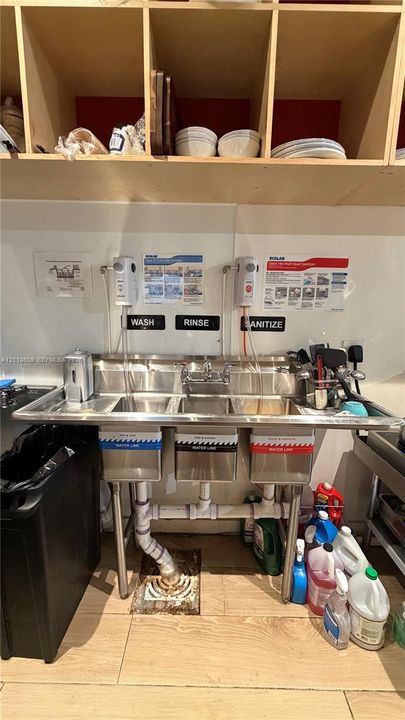 Commercial-grade triple-basin stainless steel utility sink with wall-mounted faucet and built-in open-shelf overhead storage cabinetry