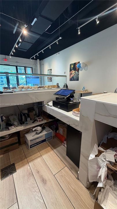 Stone-surfaced service counter with integrated glass display case, wood-finish flooring, and industrial-style ceiling track lighting