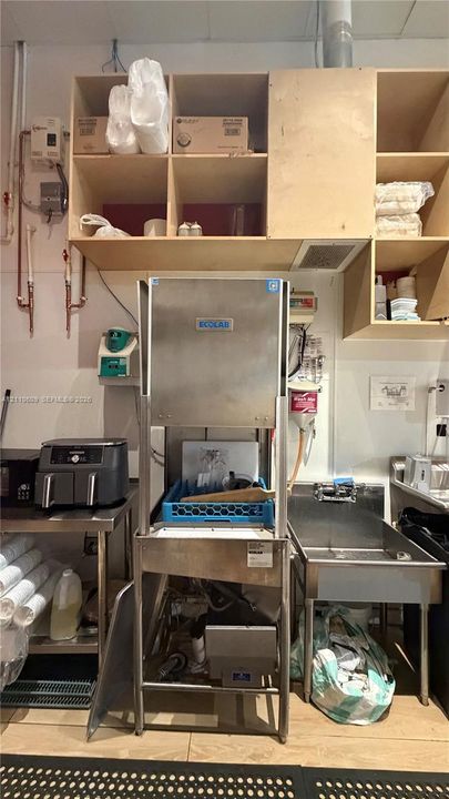 Commercial kitchen space featuring stainless steel dishwasher, stainless steel sink, and wood-finish open cabinetry