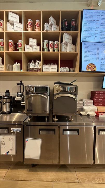Commercial-grade stainless steel refrigeration units, professional countertop appliances, built-in wooden cubby shelving, and durable tile flooring