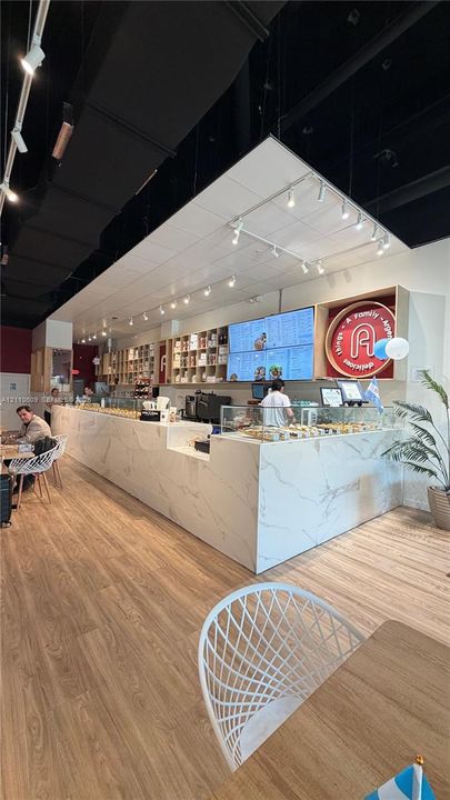 Commercial space featuring wood-finish flooring, an extensive stone-surface service counter, integrated shelving, and track lighting with an open-ceiling design