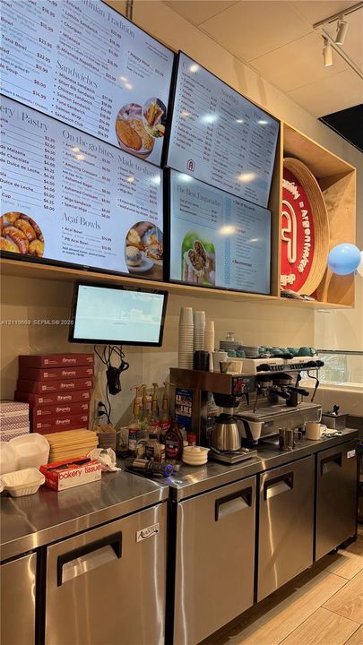 Commercial kitchen space featuring stainless steel cabinetry, integrated menu displays, and professional-grade espresso equipment