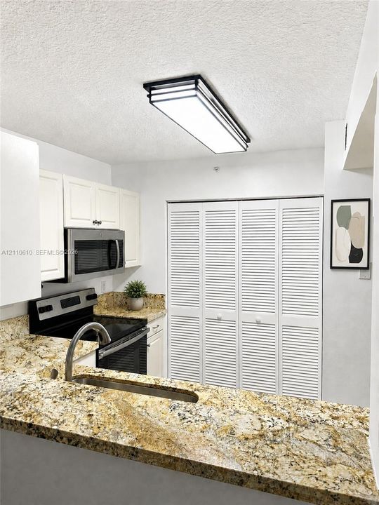 Kitchen area featuring stone countertops, white cabinetry, stainless steel microwave, black electric range, and white louvered closet doors