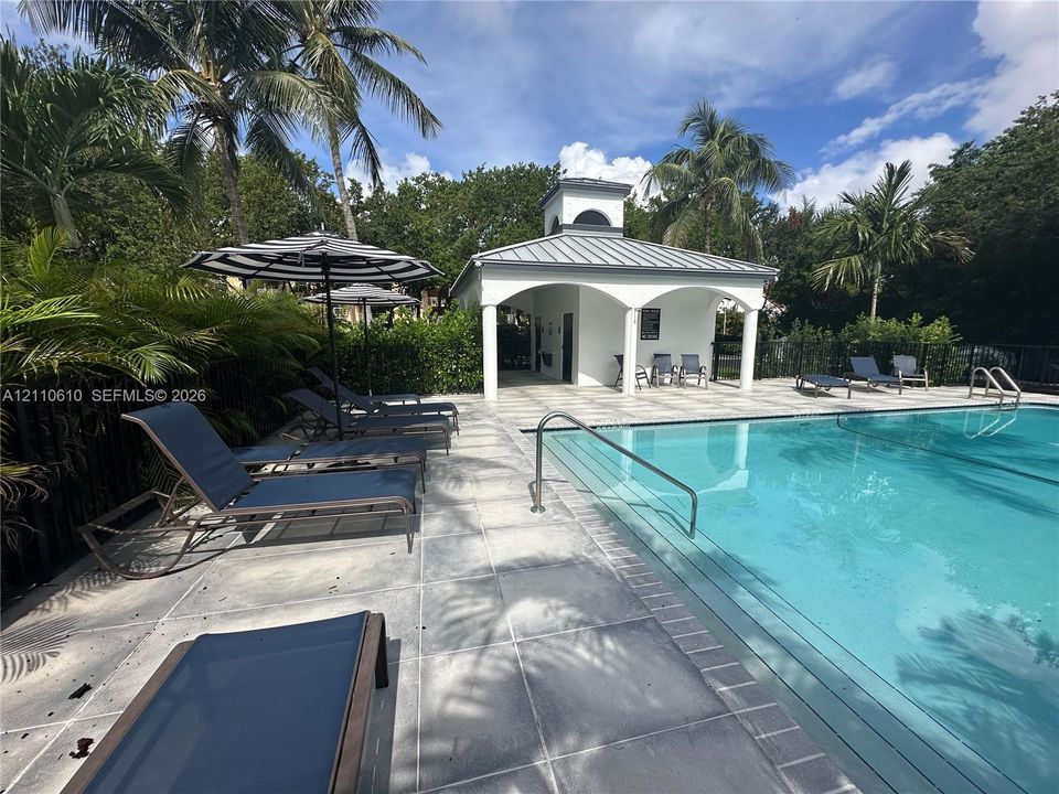 Swimming pool with a metal handrail, light-colored tile deck, and a covered pavilion featuring arched openings