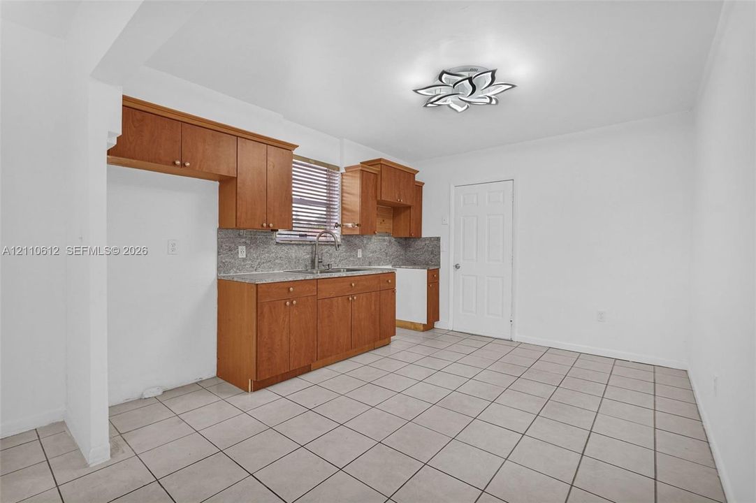 Kitchen featuring wood cabinetry, stone-finish countertops, tiled flooring, and a decorative flush-mount ceiling fixture