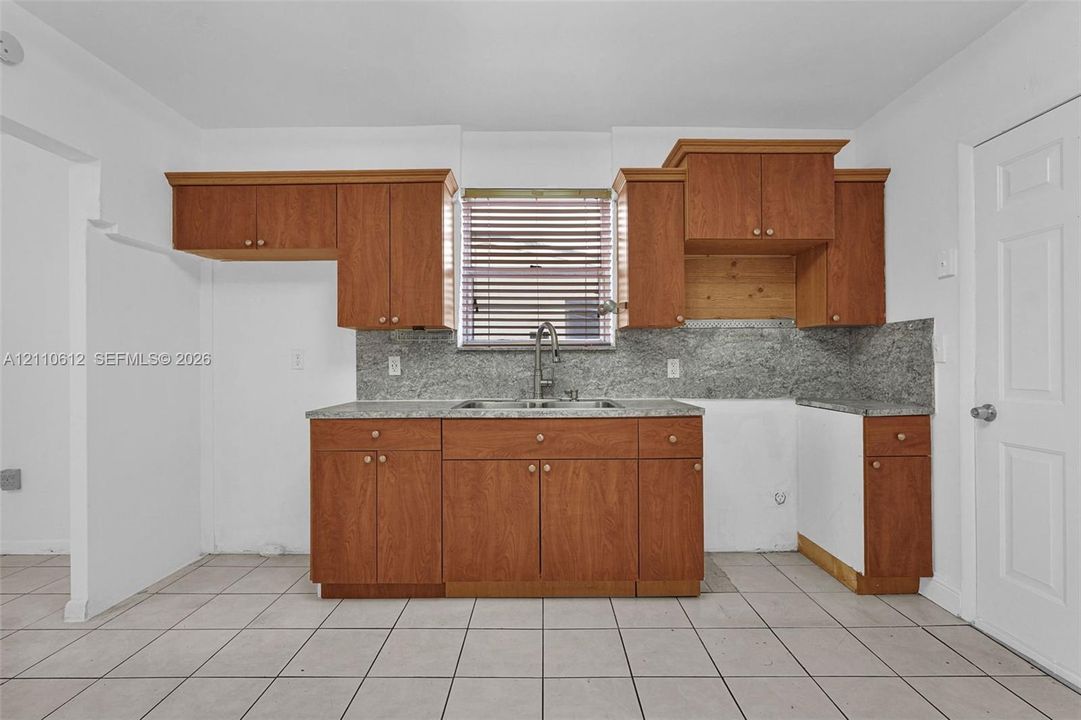 Kitchen featuring wood cabinetry, stone-surface countertops, tile flooring, and a stainless steel dual-basin sink with a gooseneck faucet