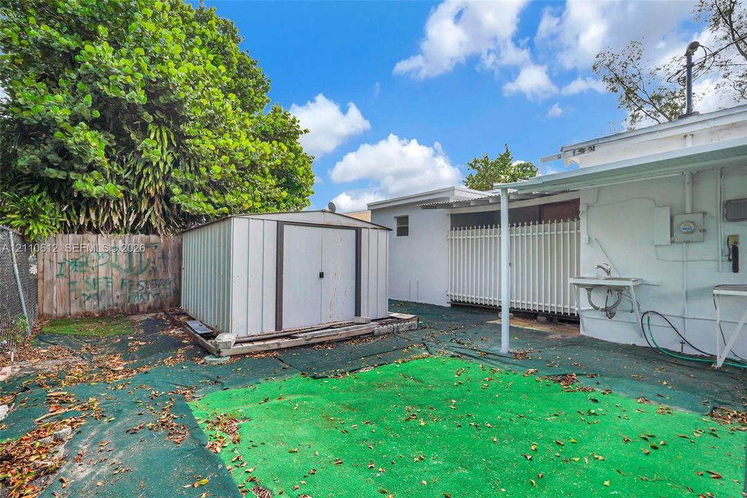 Rear exterior area featuring a metal storage shed, wood perimeter fencing, a covered patio structure, and an attached exterior utility sink
