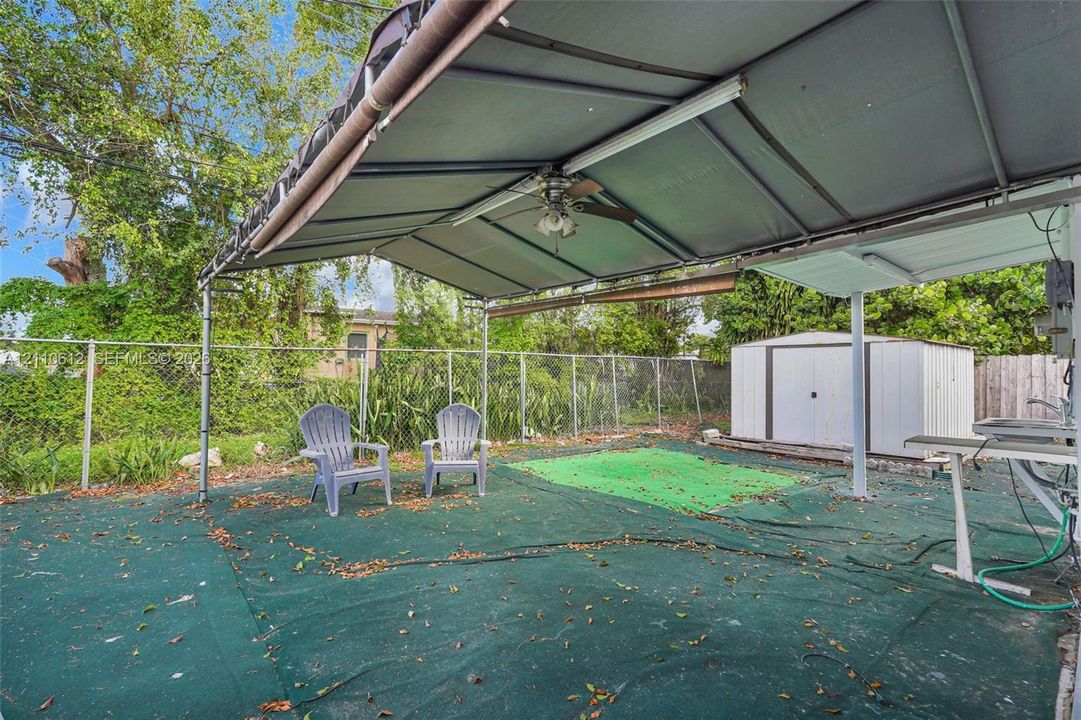 Covered patio featuring a metal frame canopy, ceiling fan, and detached storage structure situated within a fenced perimeter
