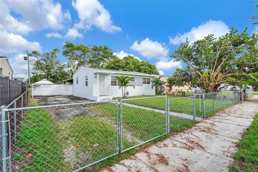 Single-story exterior with a light-colored finish, concrete driveway, fenced yard, and mature landscaping