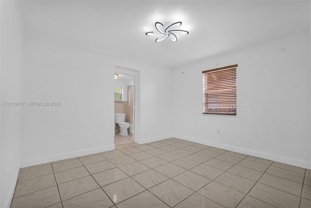 Neutral interior space featuring large-format ceramic tile flooring, a contemporary floral-style flush mount light fixture, and a window with horizontal blinds