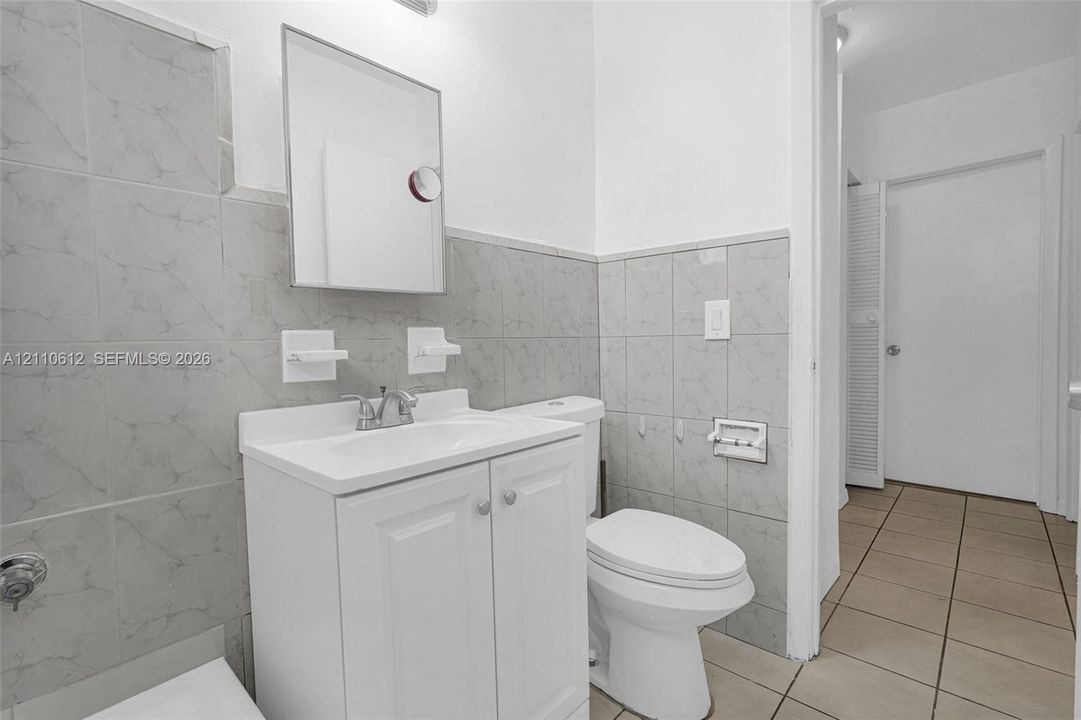 White vanity with integrated sink, rectangular wall-mounted mirror, ceramic tile wainscoting, and large-format floor tiling