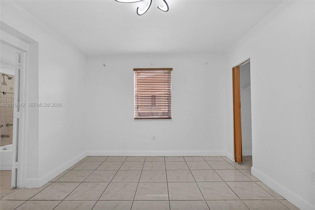 Neutral-toned tile flooring, central window with wood-slat blinds, and decorative modern ceiling light fixture