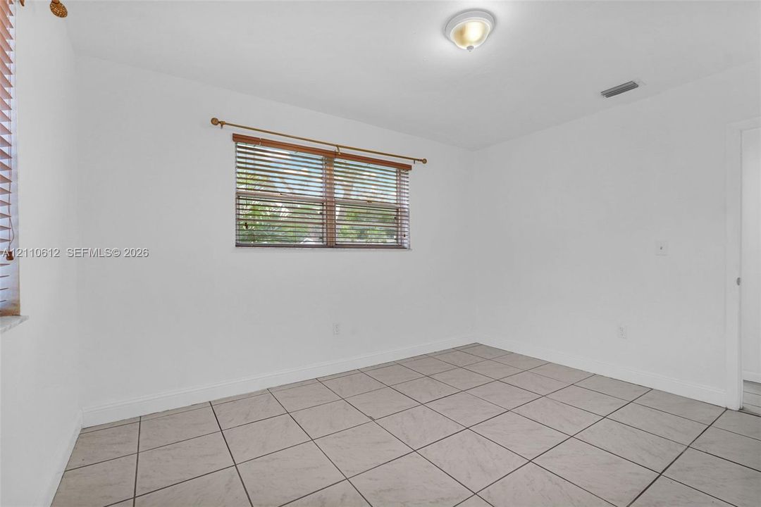 Neutral-toned ceramic tile flooring, crisp white walls, and horizontal window blinds featuring a wood-finish rod