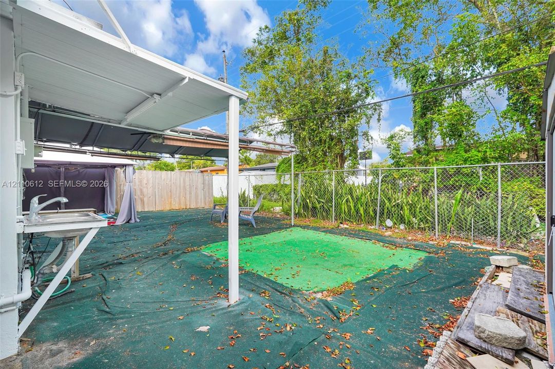 Rear exterior space featuring a covered patio, integrated utility sink, and chain-link perimeter fencing