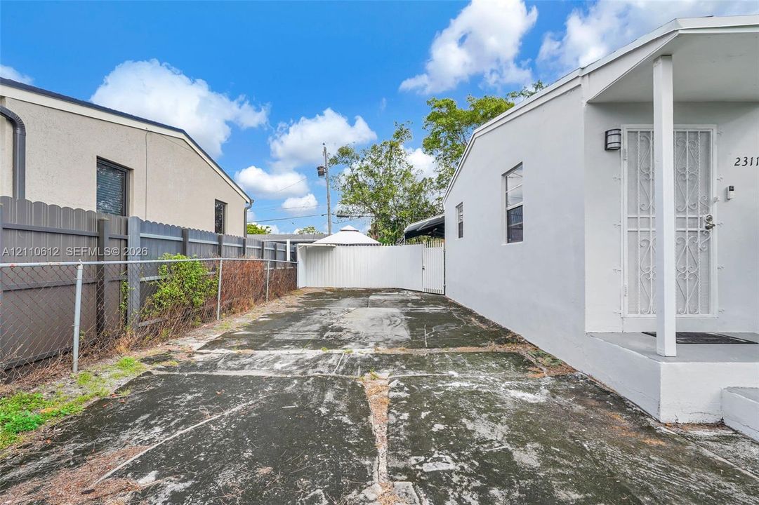 Concrete driveway, exterior wall-mounted lighting, metal security screen door, and perimeter privacy fencing