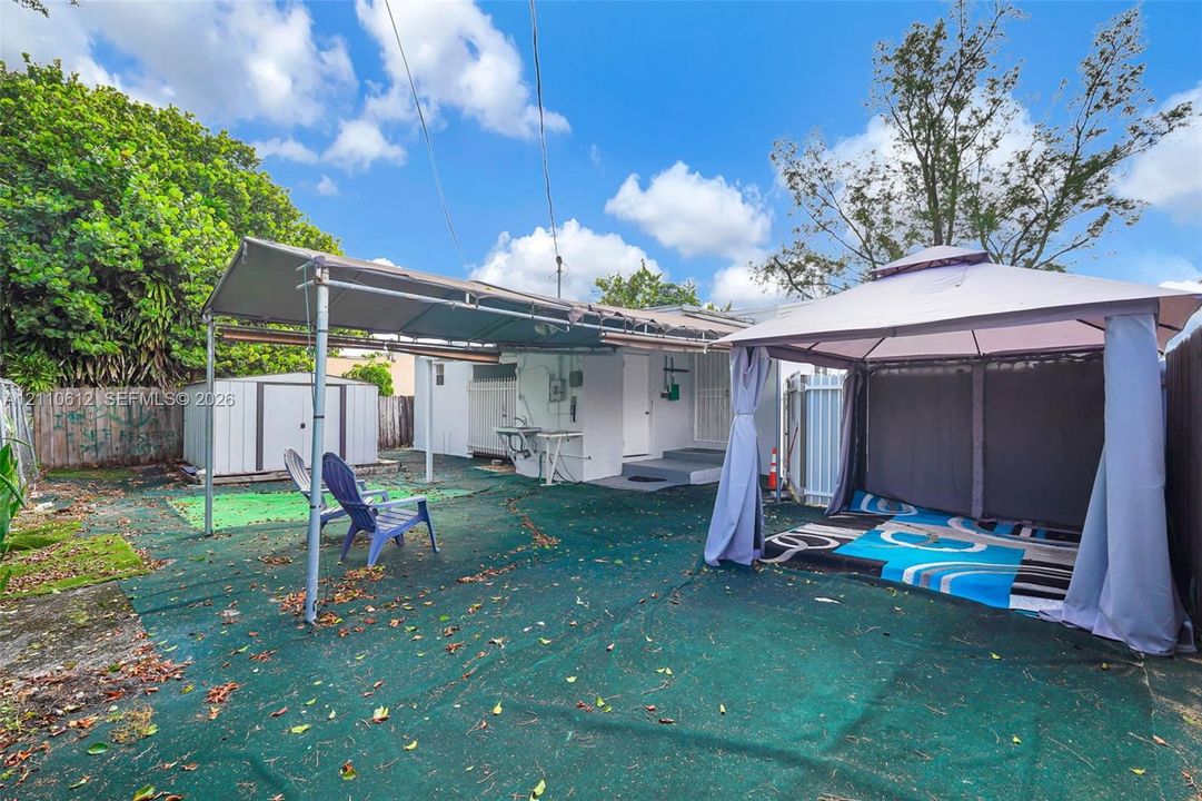 Backyard space featuring a concrete patio, metal exterior storage shed, wall-mounted utility sink, and metal-framed overhead coverings