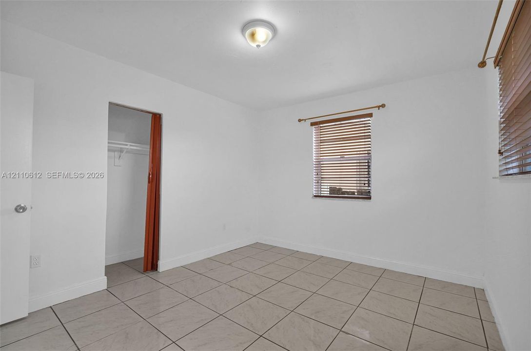 Interior space featuring neutral tile flooring, two windows with horizontal blinds, a walk-in closet, and a dome ceiling light fixture