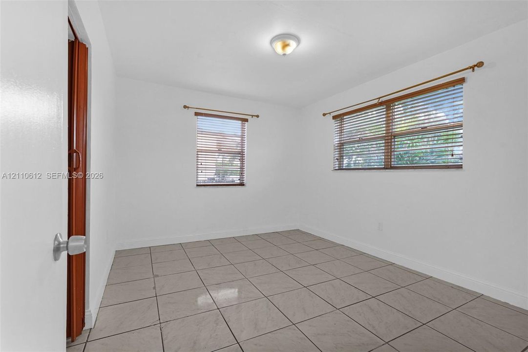 Neutral-toned tile flooring, dual windows with horizontal blinds, and a central flush-mount ceiling light fixture