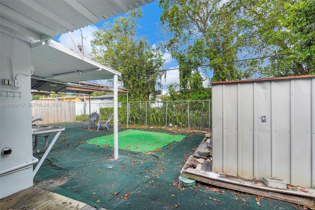 Covered patio area featuring a metal-frame structure, integrated utility sink, chain-link perimeter fencing, and an exterior metal storage unit