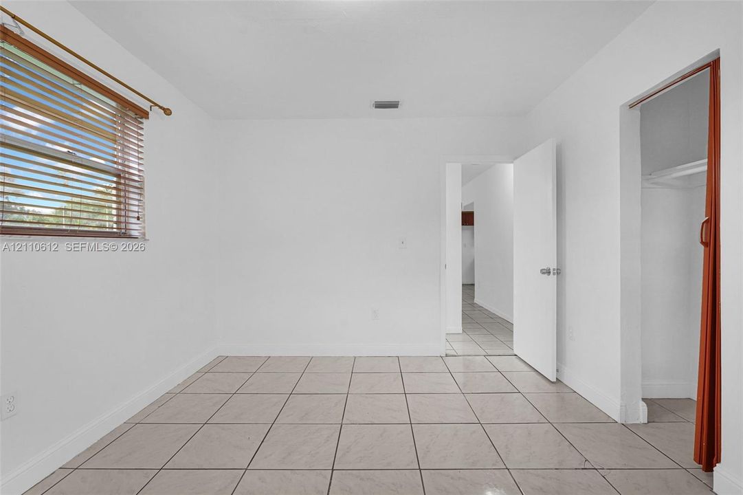 Neutral-toned tile flooring, white wall finish, window with installed horizontal blinds, and a built-in closet with sliding door hardware