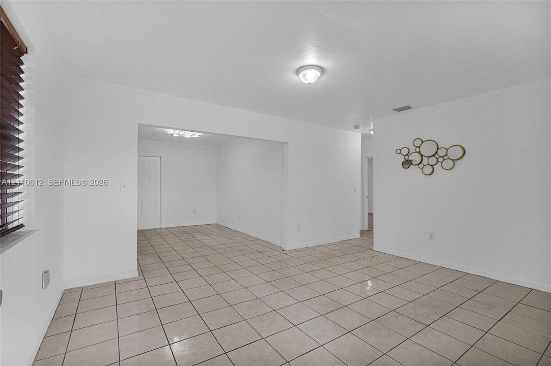 Neutral interior space featuring tile flooring, smooth-finish walls, ceiling-mounted lighting, and shuttered window treatments
