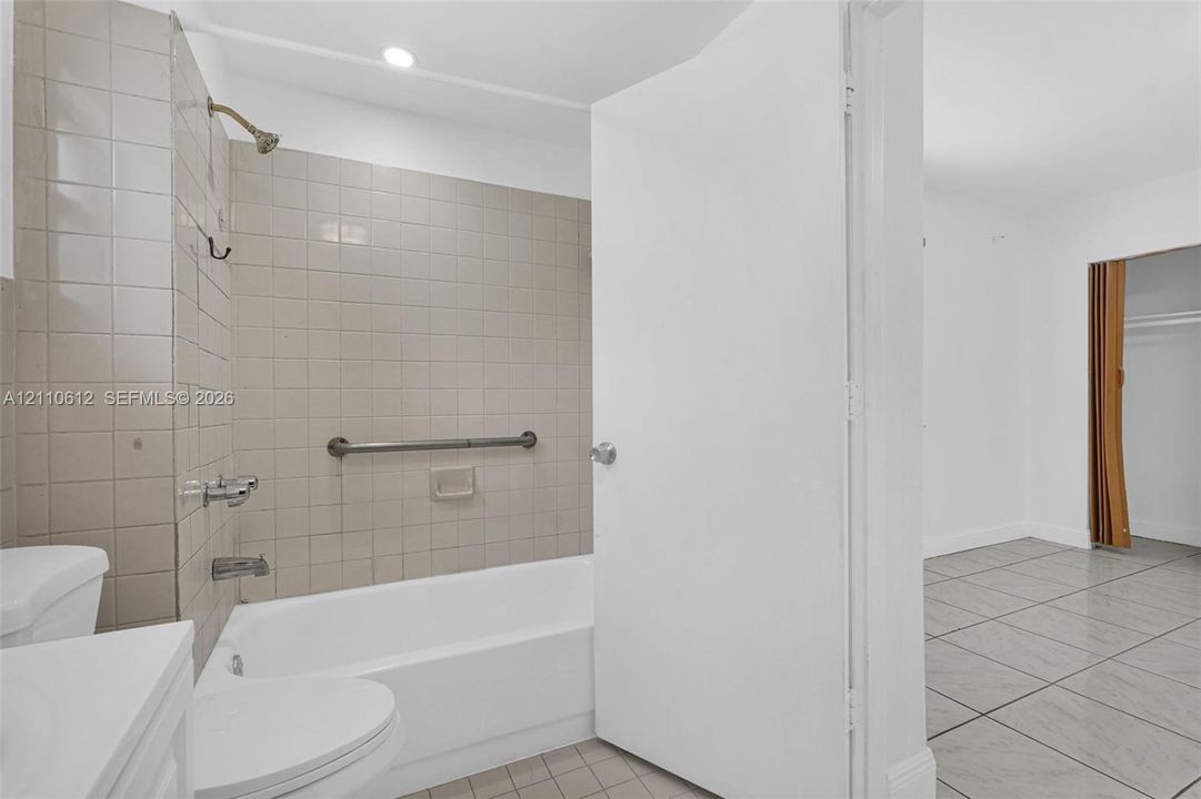Bathroom featuring neutral wall tiles, built-in bathtub, installed grab bar, chrome fixtures, and ceramic tile flooring
