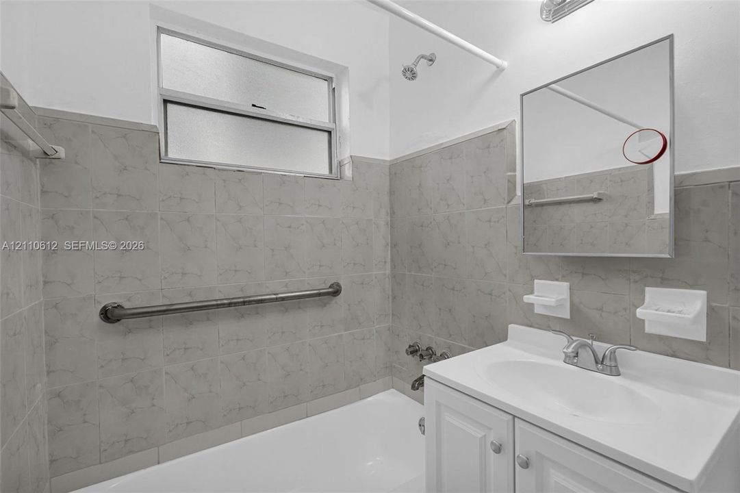 Bathroom featuring a white cabinet vanity, polished metal faucet, integrated wall-mounted soap dishes, and full-height tiled shower surround with a metal grab bar