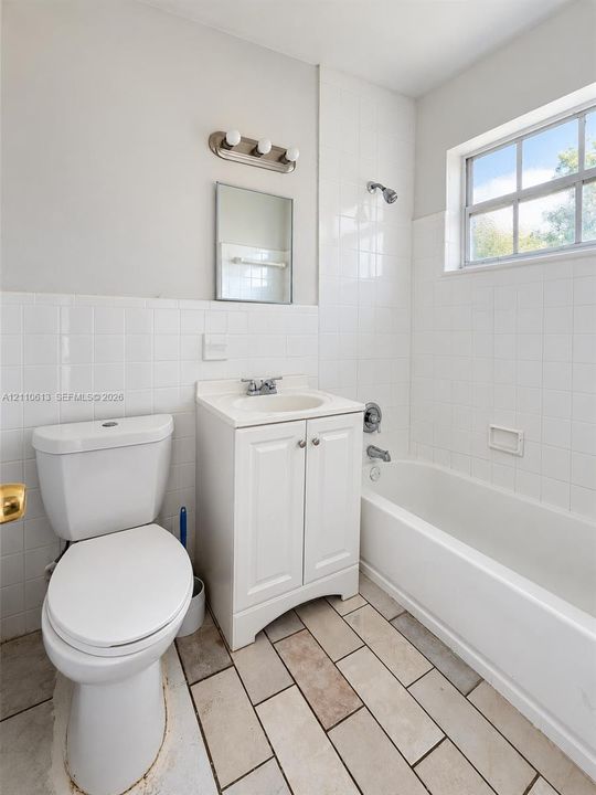 Bathroom featuring a vanity with a white cabinet, tile flooring, wall-mounted light fixture, and a shower-tub combination with white wall tile