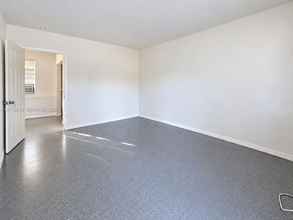 Neutral-toned interior space featuring light-reflecting epoxy flooring, smooth white walls, recessed ceiling lighting, and a six-panel interior door