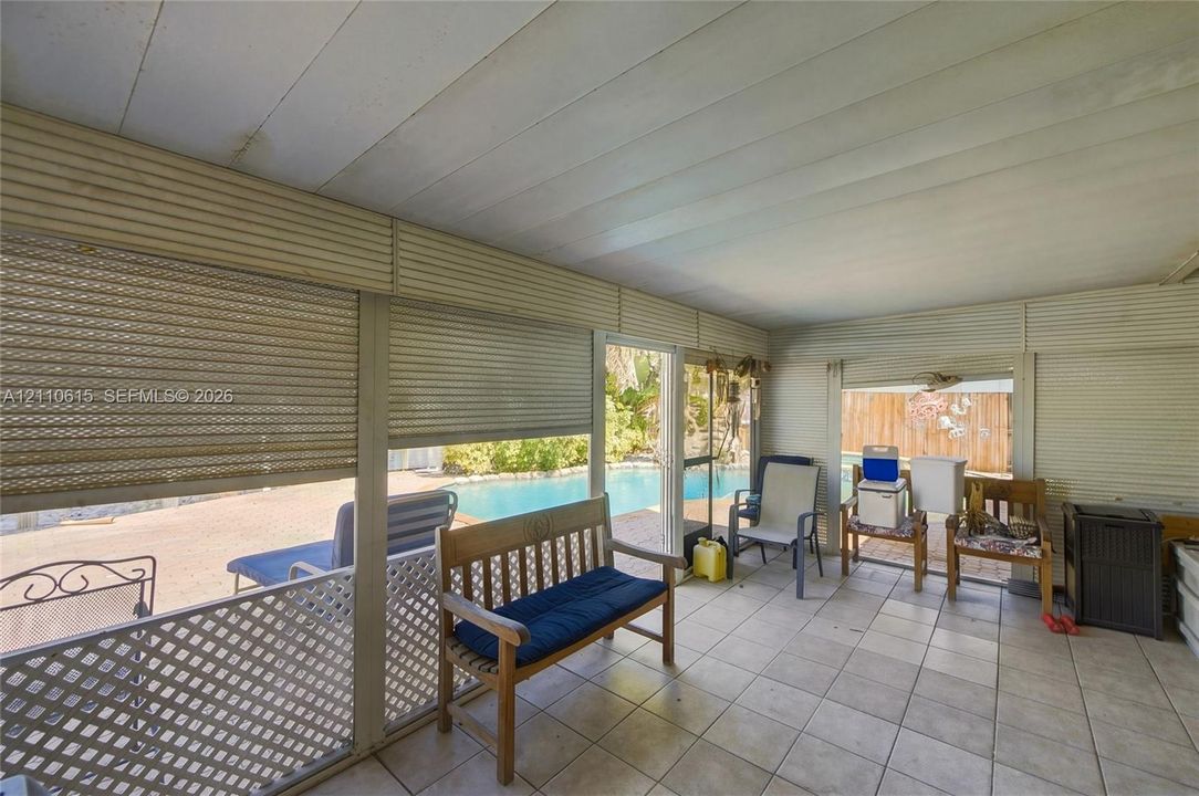 Enclosed patio featuring tile flooring, retractable metal storm shutters, and lattice screening, oriented toward an in-ground swimming pool