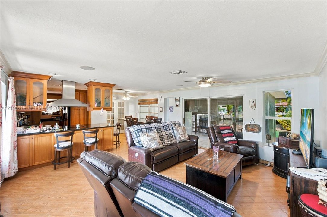 Open-concept interior featuring wood-finish cabinetry, a stainless steel range hood, tile flooring, recessed lighting, and sliding glass doors