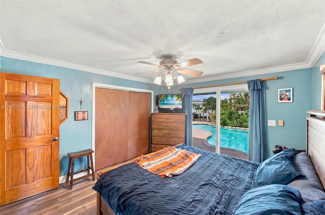Room featuring wood-finish flooring, ceiling fan with integrated lighting, sliding glass door, and built-in closet with wood-grain panels