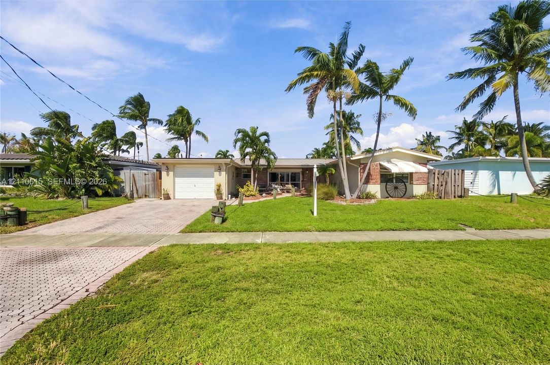 Single-story exterior featuring a brick facade, paved driveway, one-car garage, and established palm trees