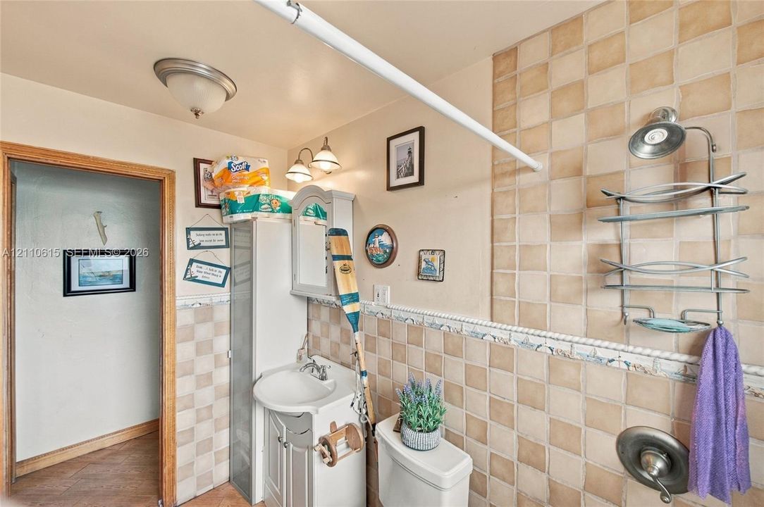Bathroom featuring square ceramic wall tiling with a decorative border, pedestal vanity with a sink, built-in storage cabinet, and a single-handle shower valve