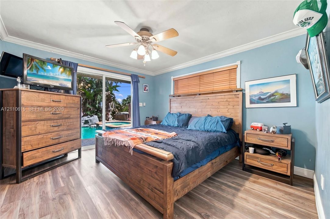 Wood-finish flooring, crown molding, multi-blade ceiling fan with integrated lighting, and sliding glass doors with wood-slat blinds