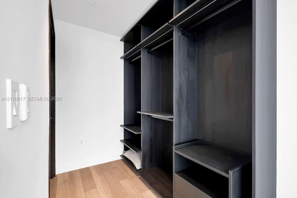 Custom dark-finish built-in cabinetry featuring multi-level shelving, hanging rods, and integrated drawers, paired with light-tone wood-finish flooring