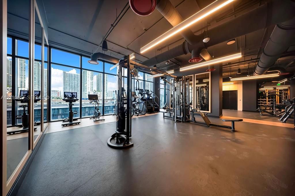 Fitness center featuring floor-to-ceiling windows, industrial-style exposed ductwork, recessed linear lighting, and wall-to-wall mirrors
