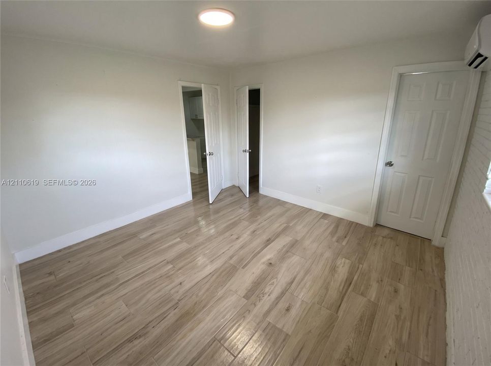 Interior space featuring wood-finish flooring, two-panel interior doors, flush-mount ceiling lighting, and a wall-mounted climate control unit