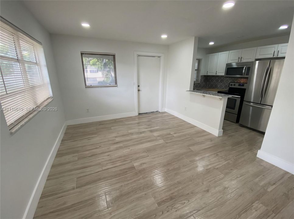 Wood-finish tile flooring, recessed ceiling lighting, kitchen featuring white cabinetry, stone-surfaced breakfast bar, and stainless steel appliances