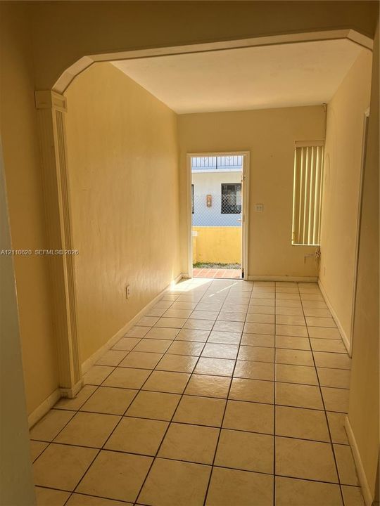 Interior space featuring large-format ceramic tile flooring, arched architectural detail with column molding, and vertical window blinds